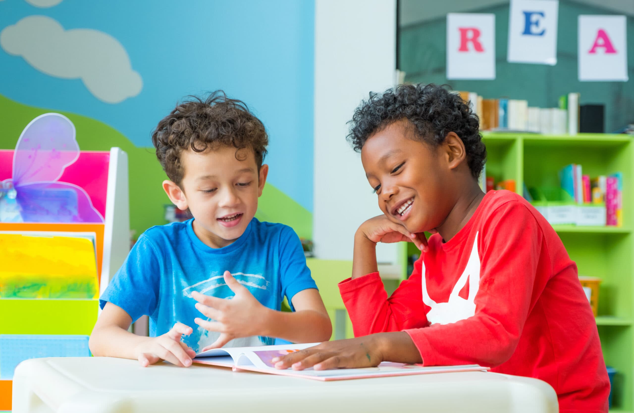 Two boy kid sit on table and reading tale book in preschool lib